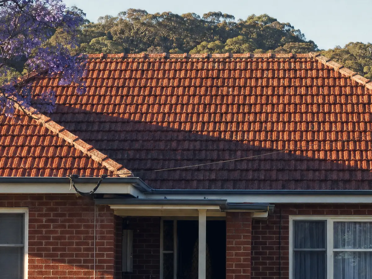 A post-war Cardiff brick-and-tile home, its original terracotta tile roof and weathered ridge capping under a jacaranda